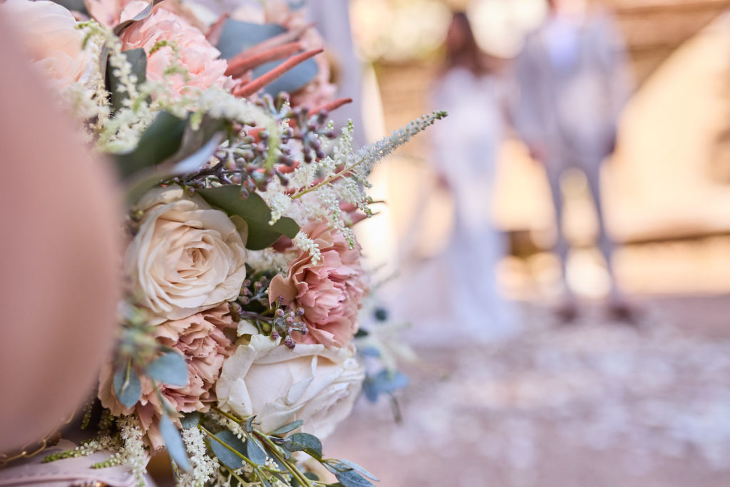 Close-up of a bouquet of blush roses with the ceremony blurred behind