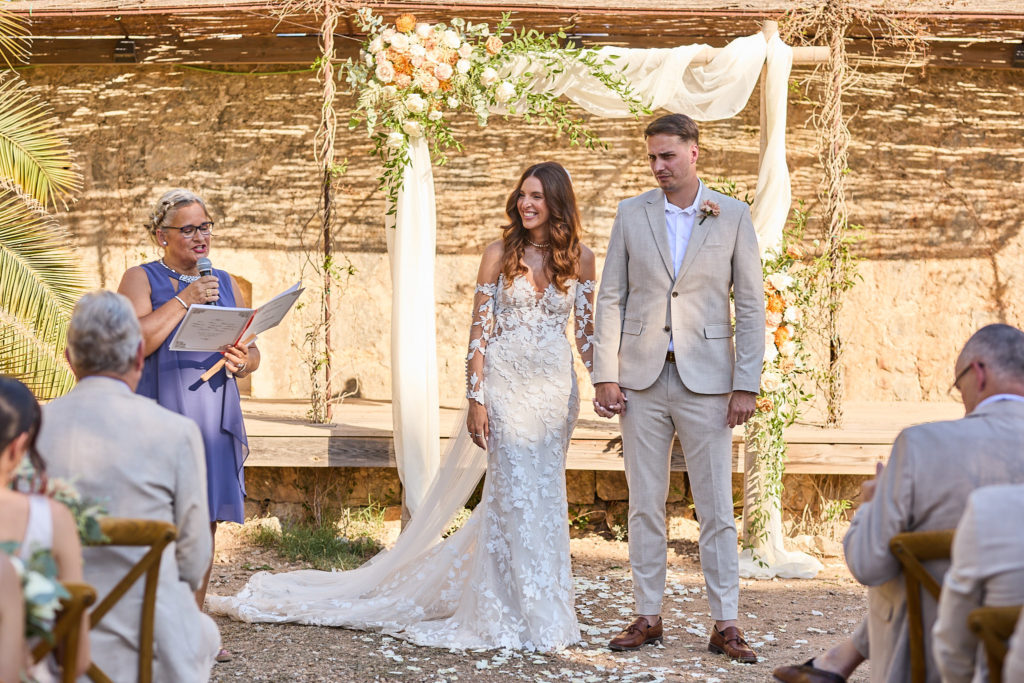 Bride and groom standing with the celebrant under a flower arch at Son Boronat
