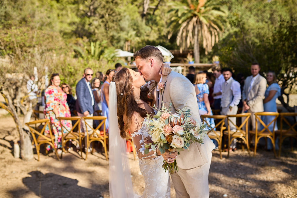 Bride and groom kissing at the end of the aisle as guests cheer