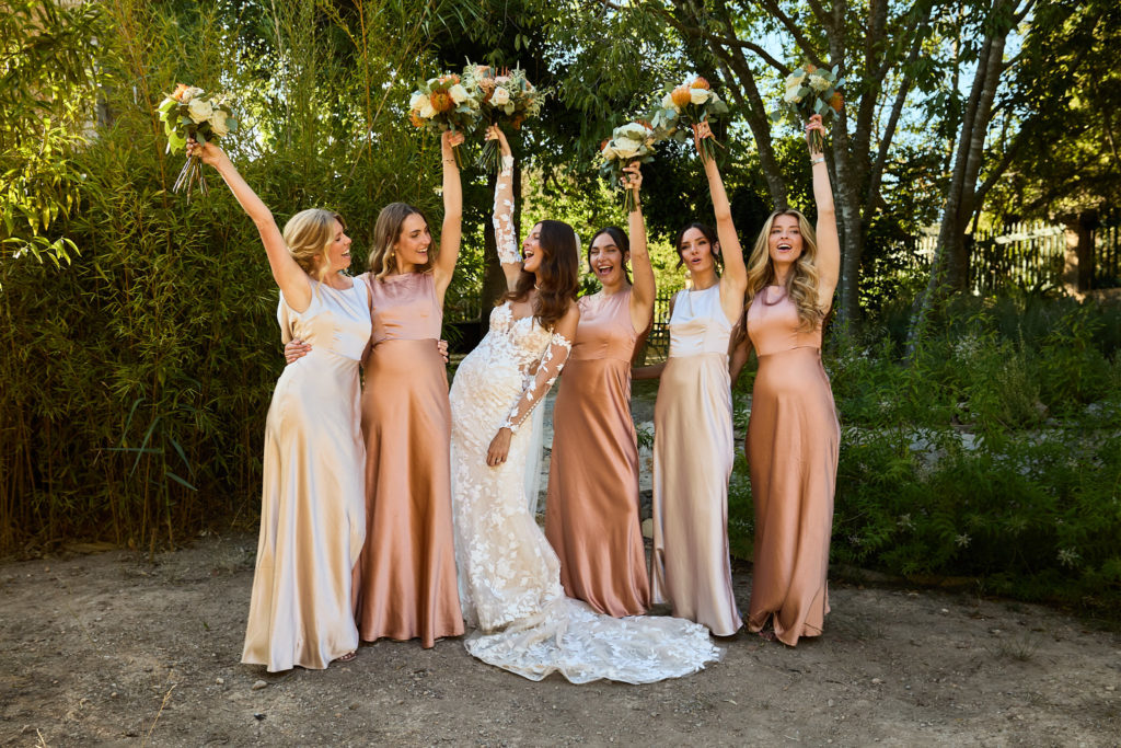 Bride and bridesmaids in peach dresses holding their bouquets in the air