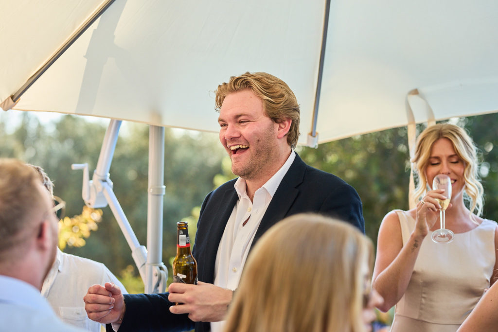 Wedding guest laughing with a drink under a parasol