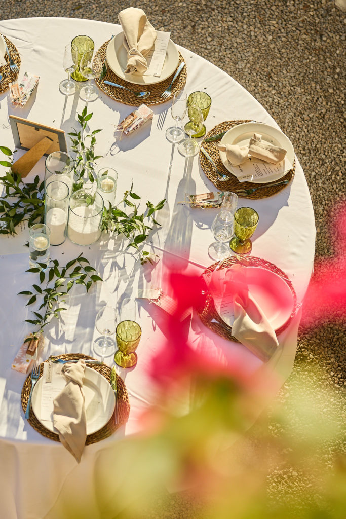 Wedding table with gold-rimmed plates and green glassware, seen from above past bougainvillea