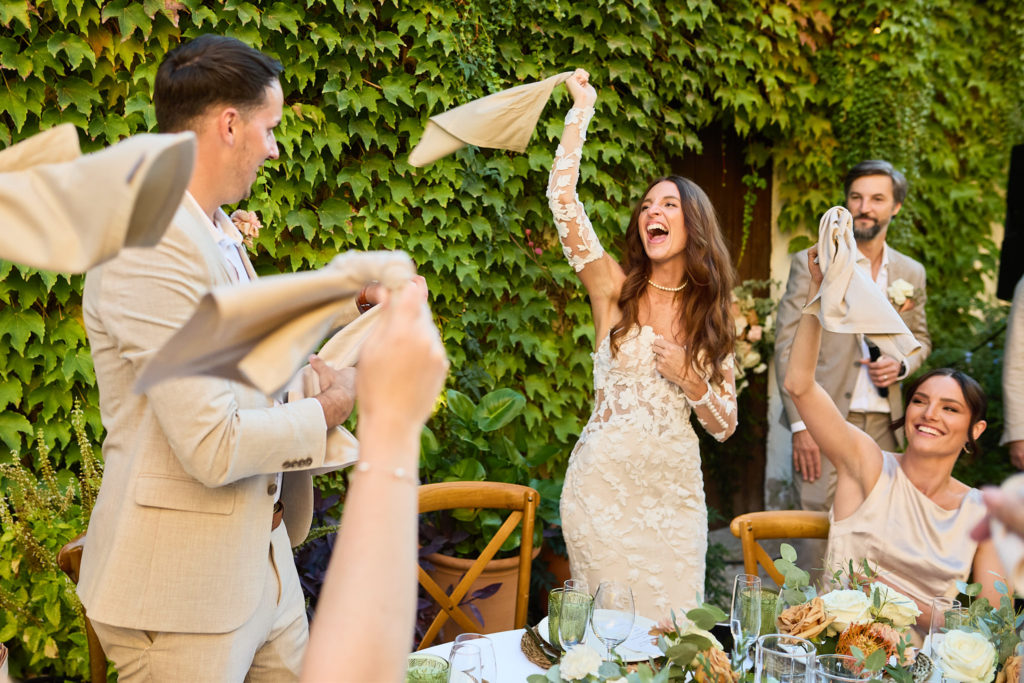 Bride and groom laughing as guests wave napkins to welcome them to dinner
