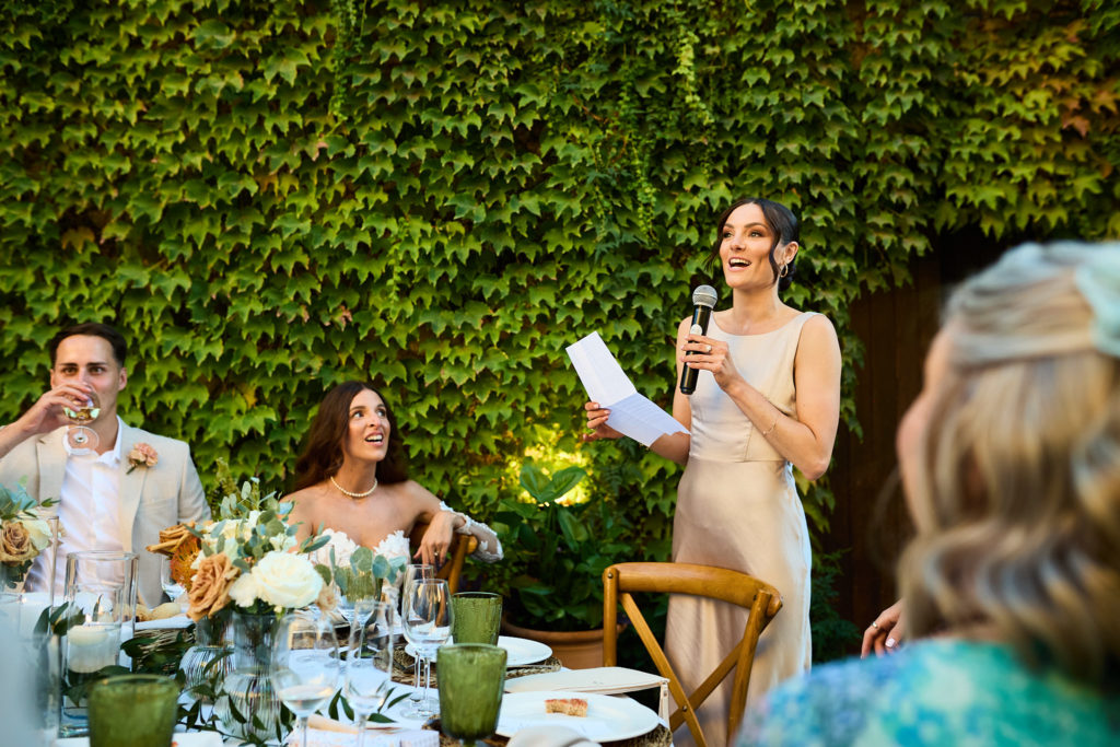 Bridesmaid giving a speech in front of an ivy-covered wall
