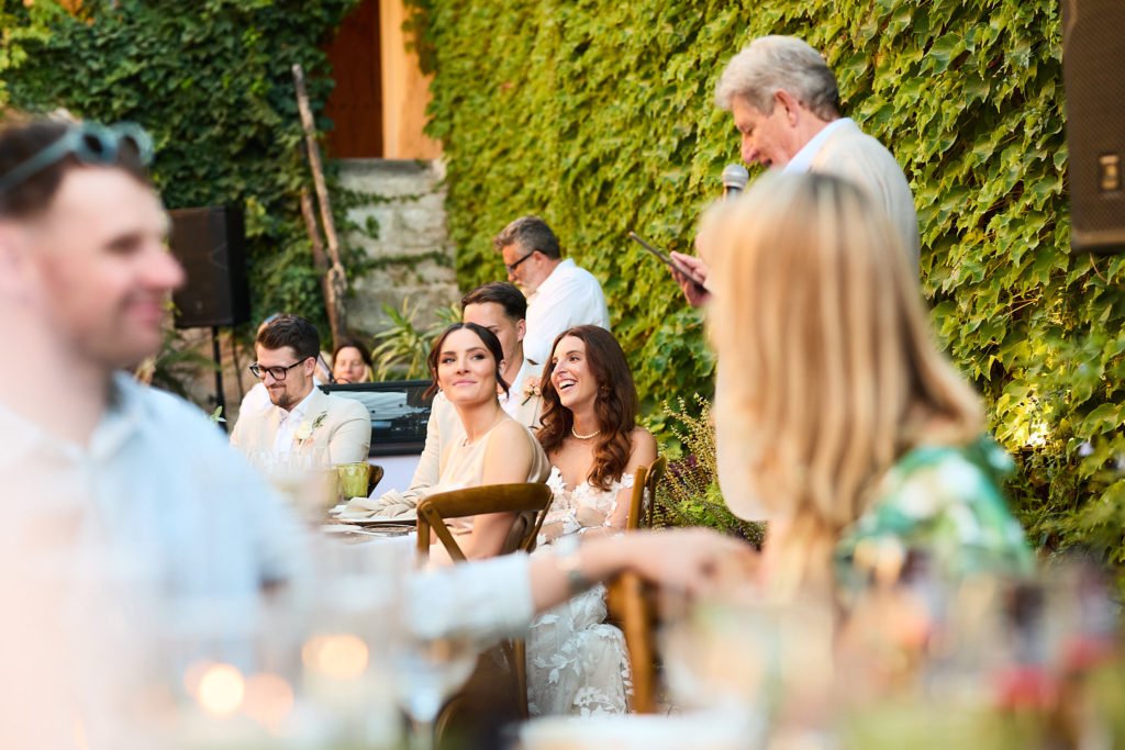Bride and guests laughing during a speech in the courtyard