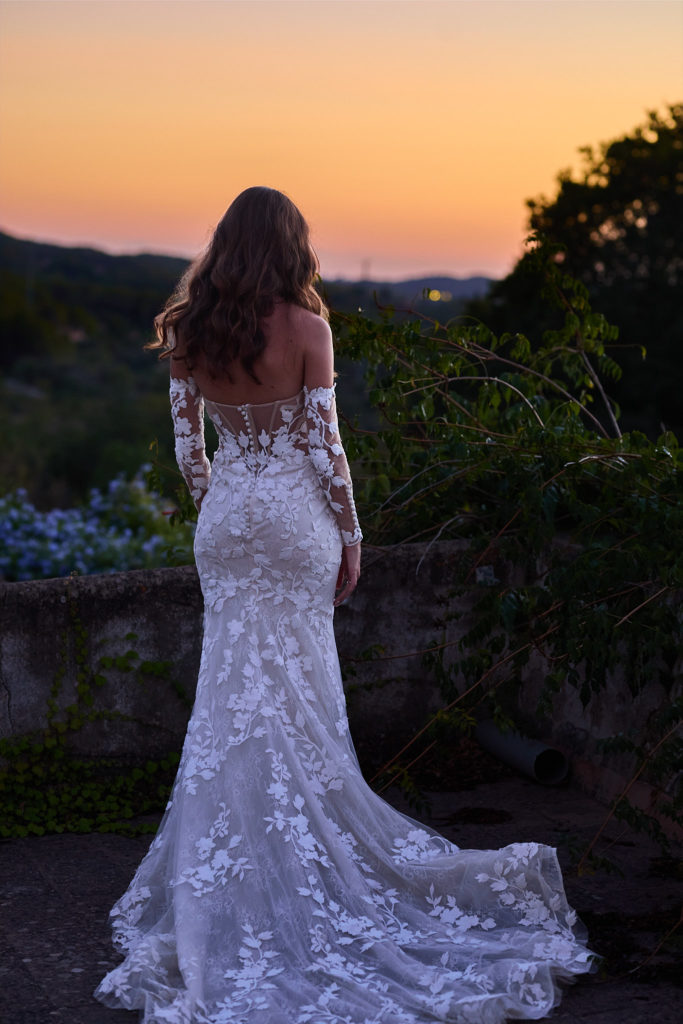 Bride from behind in her lace wedding dress looking out at the sunset over Mallorca