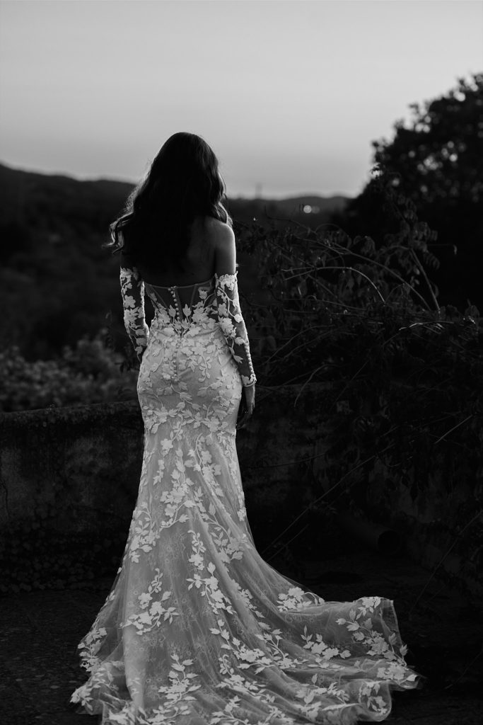 Black and white photo of the bride from behind looking out over the hills at dusk