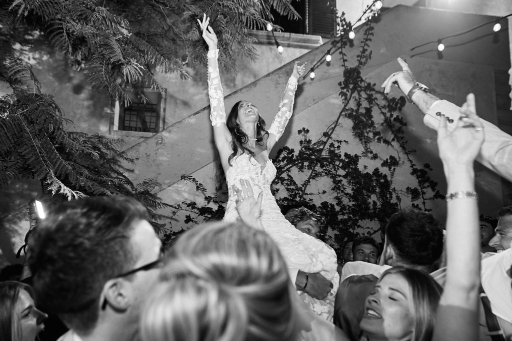 Black and white photo of the bride held aloft above the crowd on the dance floor