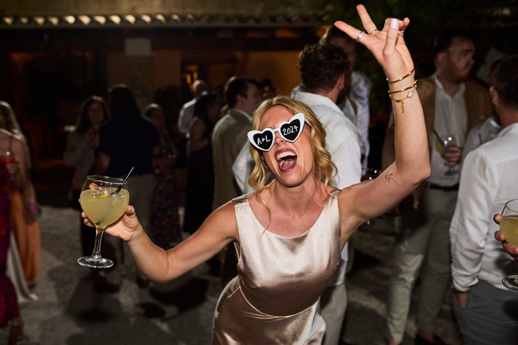 Wedding guest in white sunglasses dancing with a drink in her hand