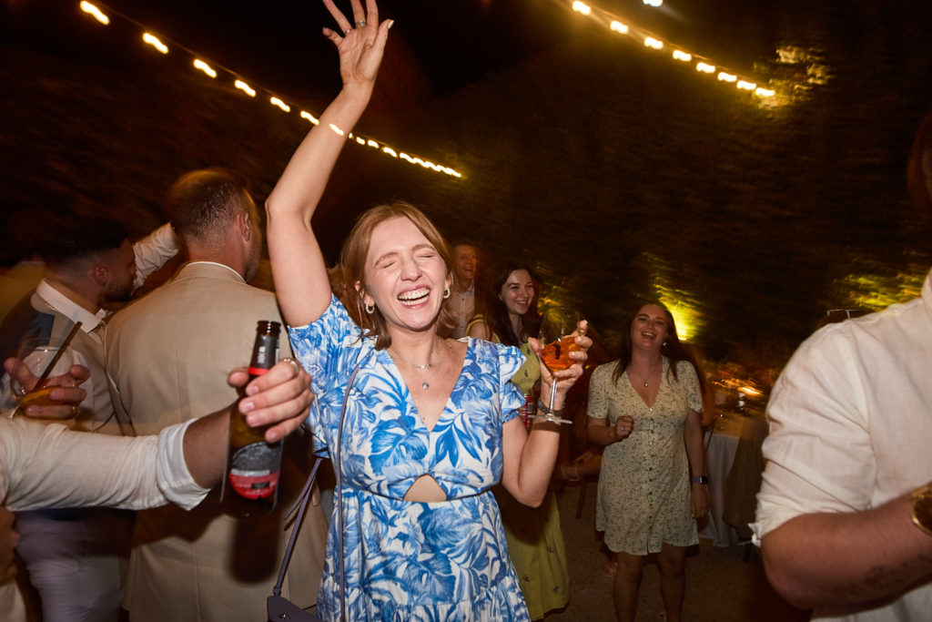 Wedding guest in a blue floral dress dancing with her arm in the air