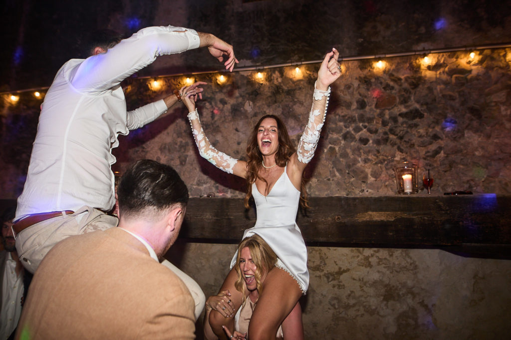 Guests dancing on each other's shoulders under festoon lights