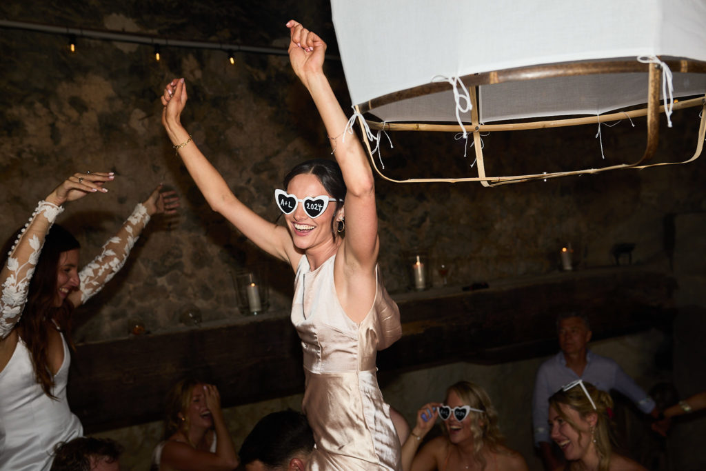 Guest in white sunglasses dancing on someone's shoulders with her arms raised