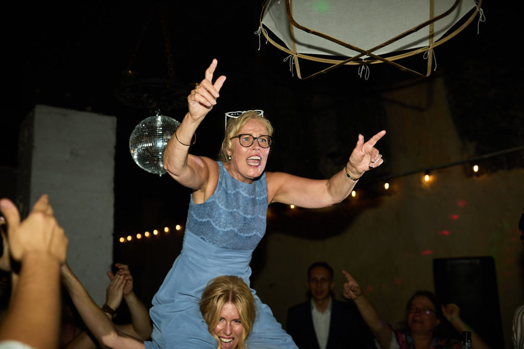 Guest in a blue dress on someone's shoulders, pointing at the camera