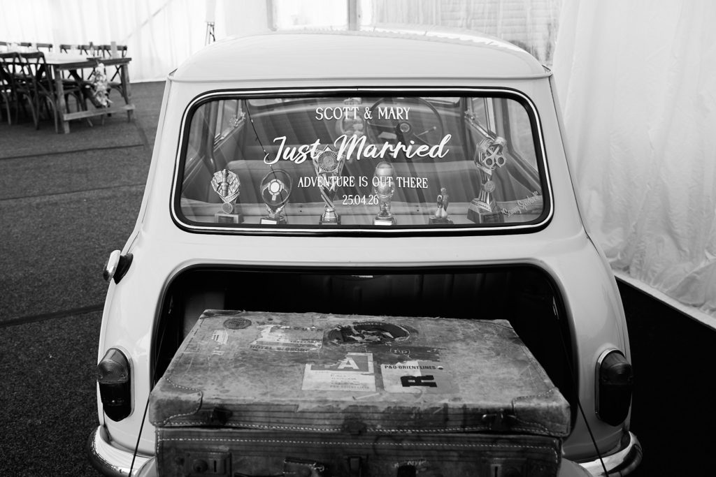 Black and white rear view of a classic Mini with "Just Married" on the window and a vintage suitcase in the boot