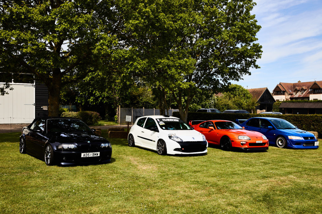 Row of four modified cars in black, white, orange and blue parked on the grass