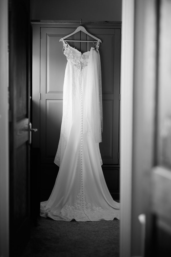 Black and white photo of a wedding dress hanging on a door