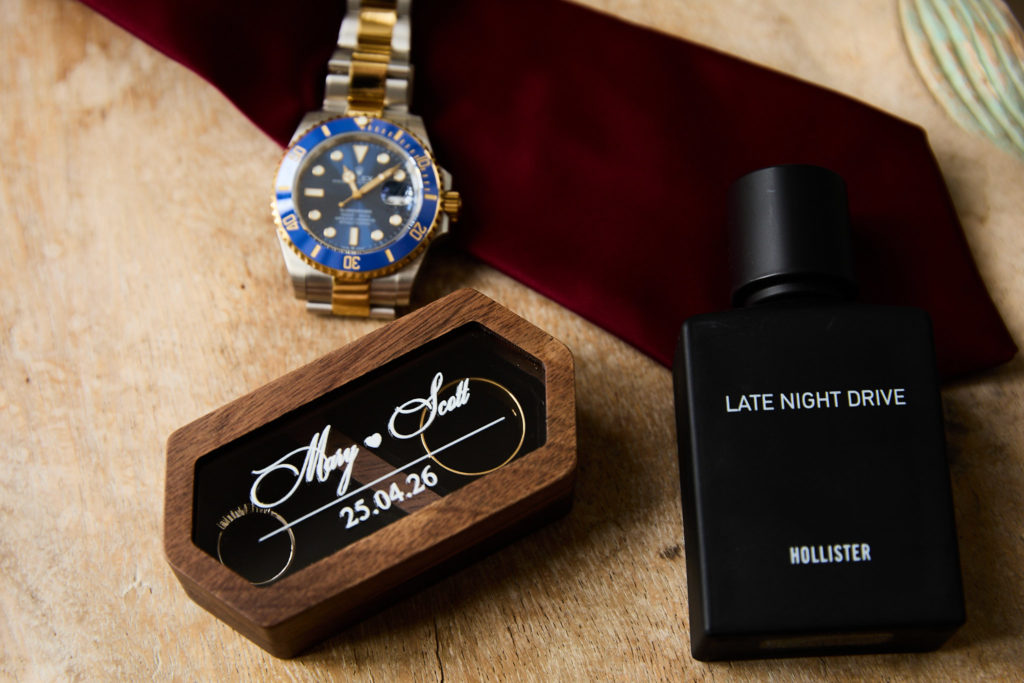 Groom's watch, burgundy tie, cufflink box and aftershave laid out on wood