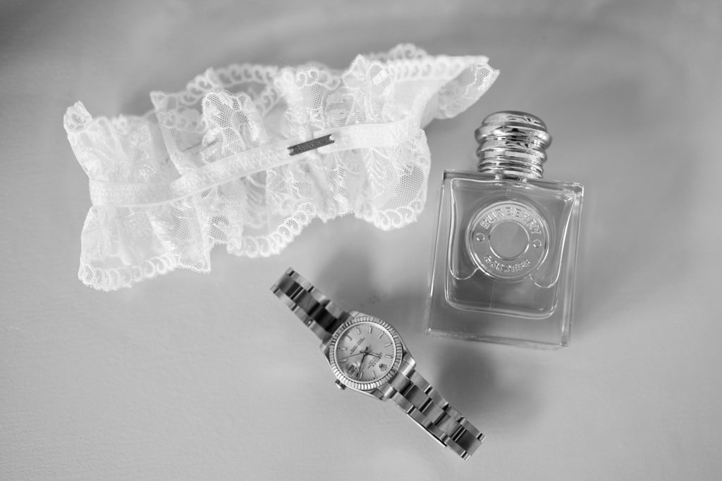 Black and white photo of the bride's lace garter, watch and perfume bottle
