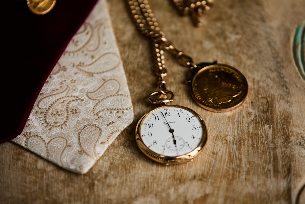 Gold pocket watch and chain beside a patterned cream tie