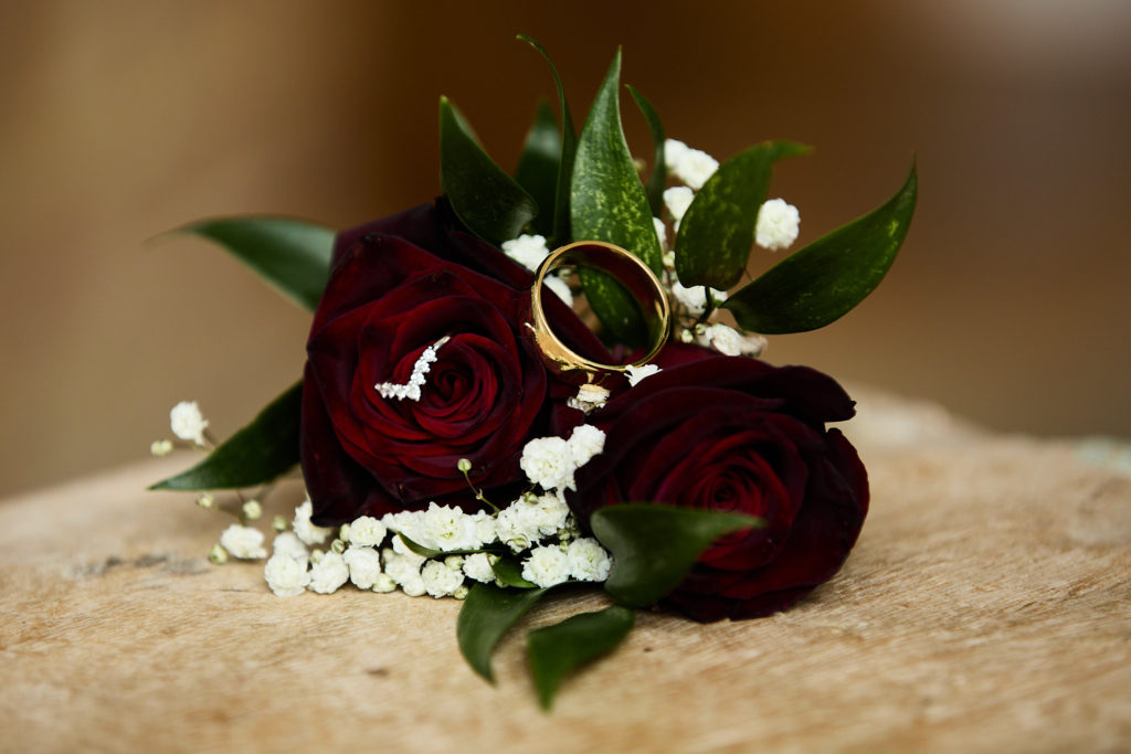 Wedding rings resting on a red rose buttonhole with gypsophila