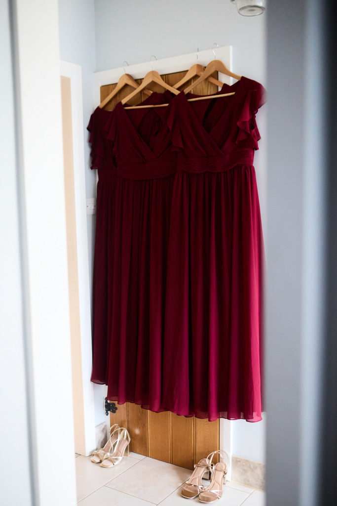 Burgundy bridesmaid dress hanging in a doorway with shoes below