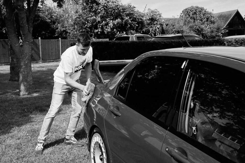 Black and white photo of a man polishing a car on the wedding morning