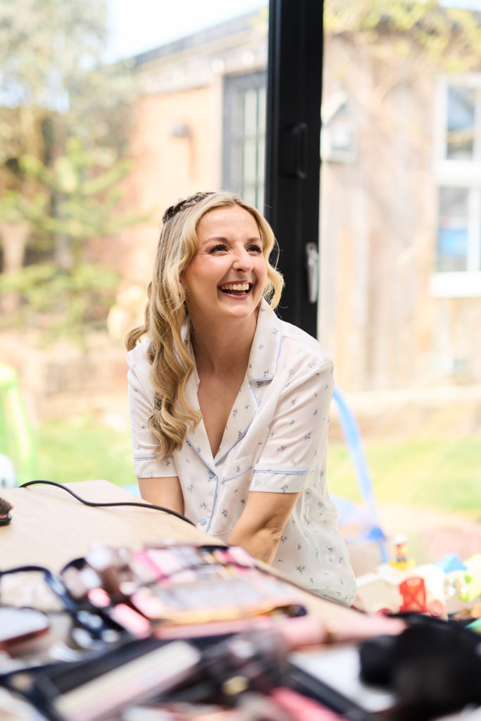 Bride laughing at the make-up table beside a sunny window