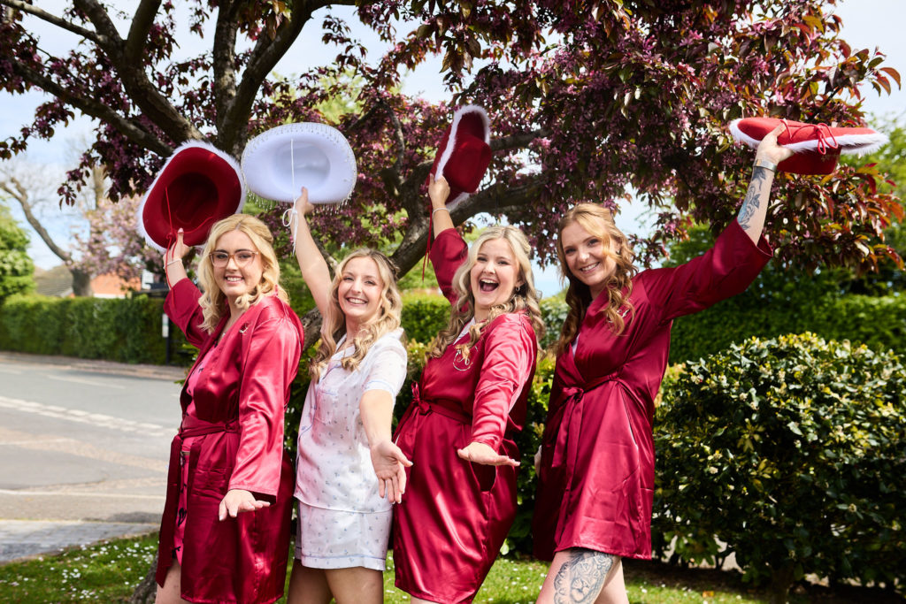 Bride and bridesmaids in burgundy robes throwing cowboy hats in the air in South Fambridge, Essex