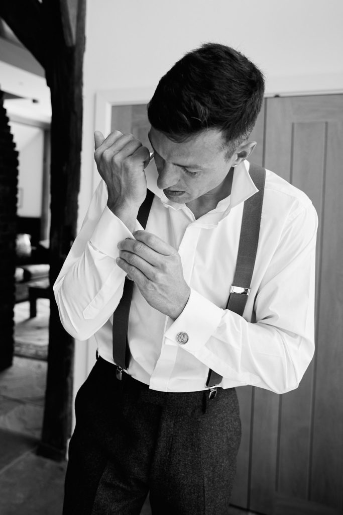 Black and white photo of the groom in braces fastening his shirt cuff