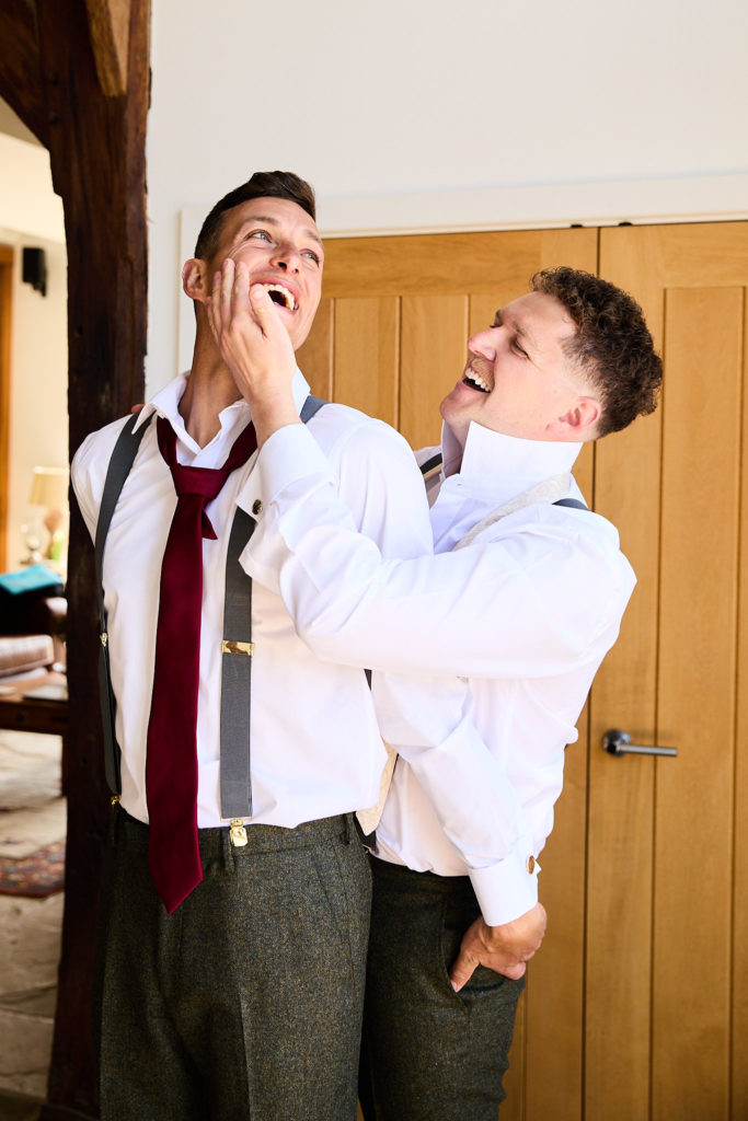 Groomsman adjusting the groom's collar as the groom laughs