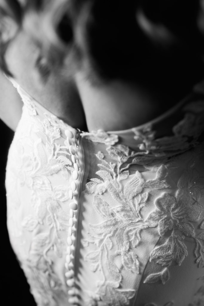 Black and white close-up of the buttons on the back of a lace wedding dress