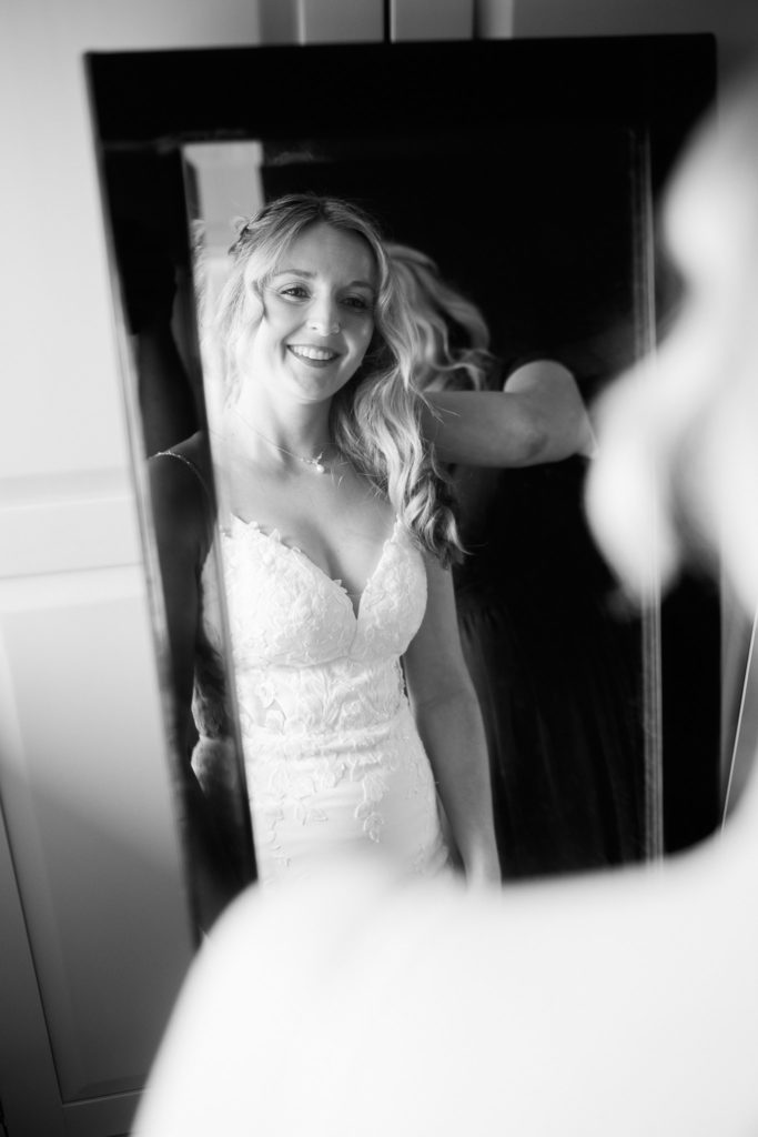 Black and white photo of the bride smiling at her reflection in a mirror