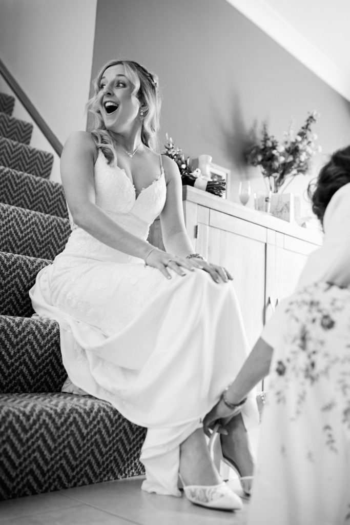 Black and white photo of the bride laughing on the stairs while her shoes are fastened