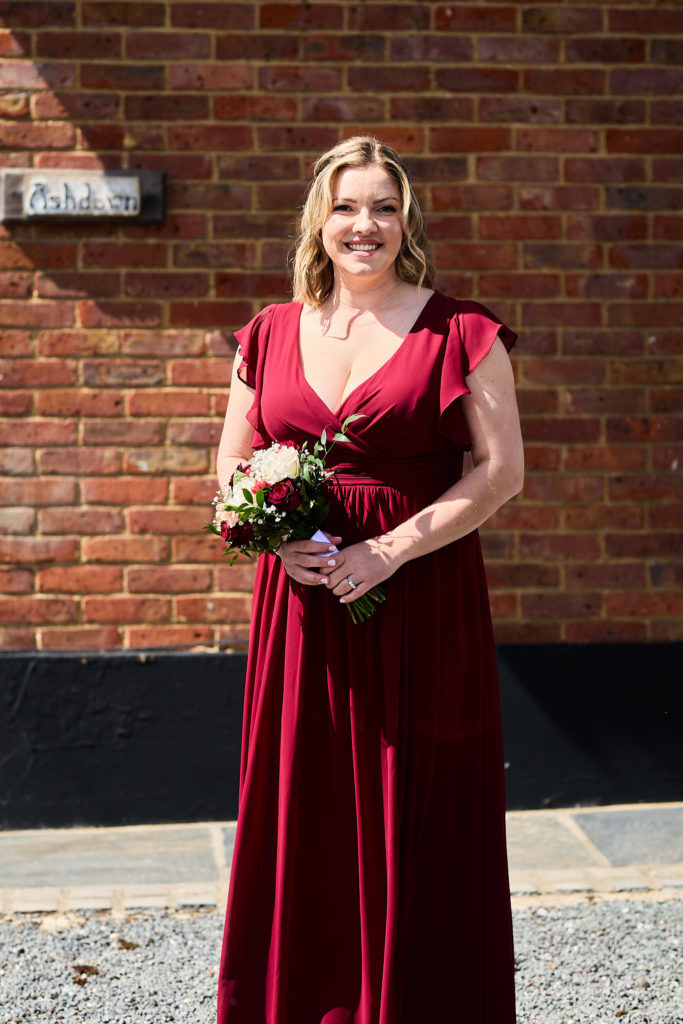 Bridesmaid in a burgundy dress holding a bouquet in front of a brick wall