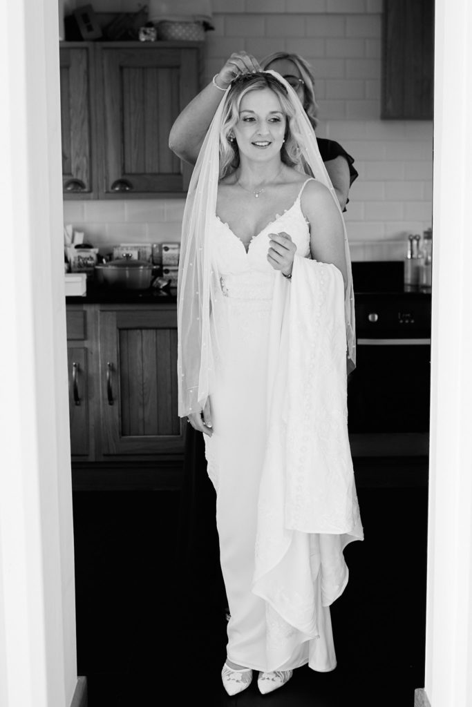 Black and white photo of the bride lifting her veil in a doorway