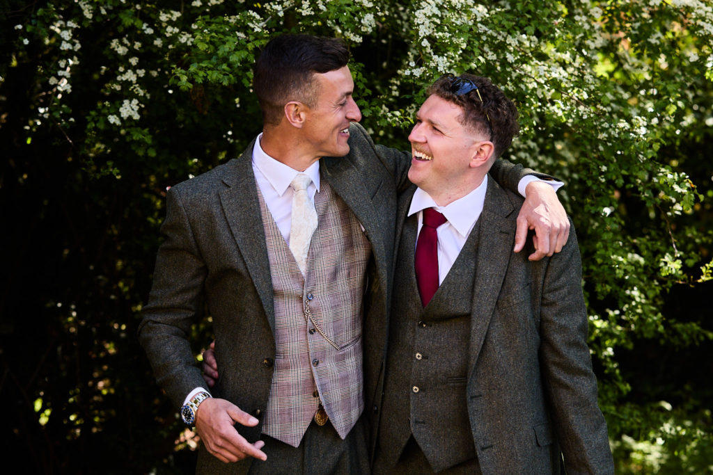 Groom and best man in tweed suits laughing arm in arm