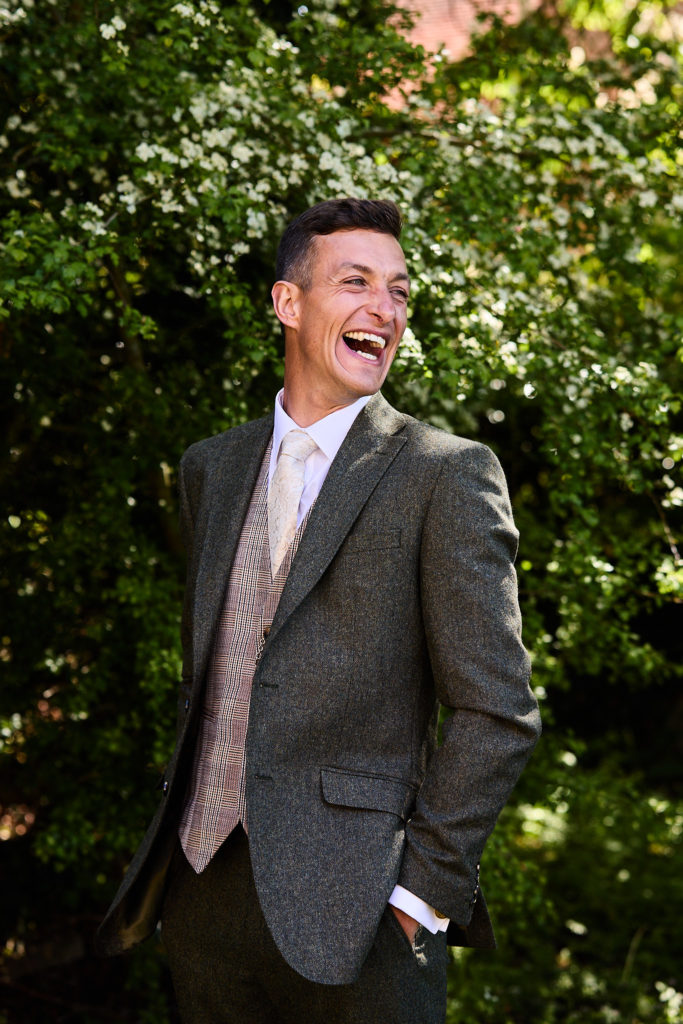 Groom laughing in a tweed jacket in the sunshine