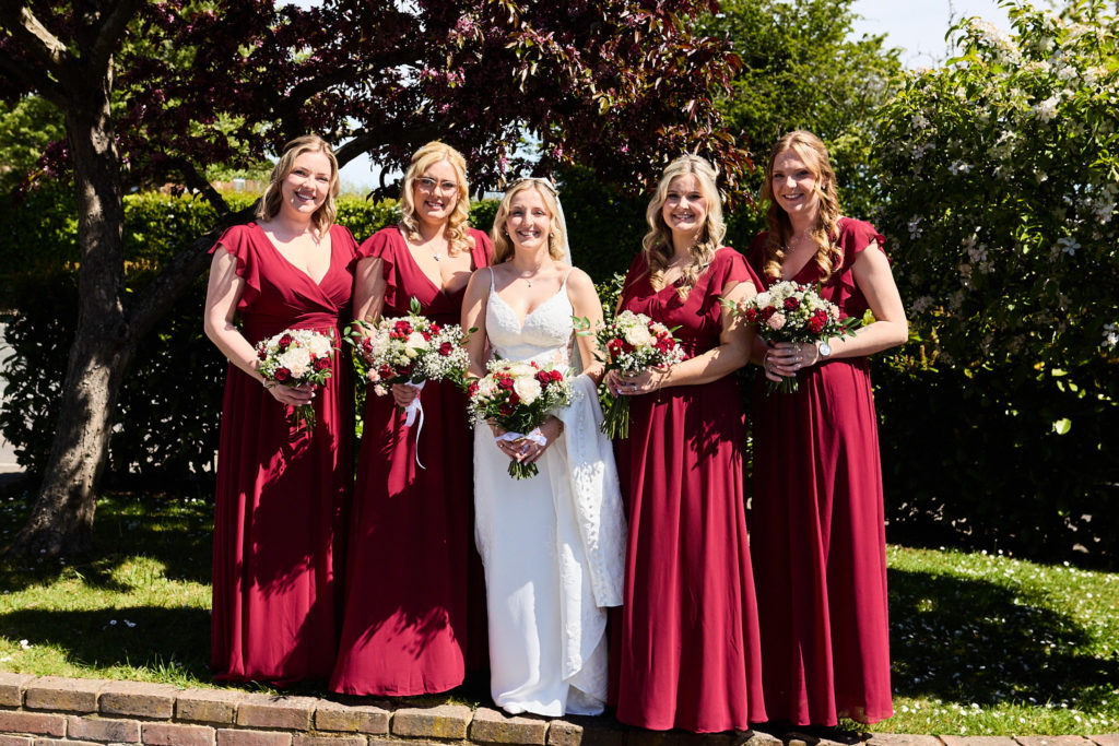 Bride with four bridesmaids in burgundy dresses in a garden