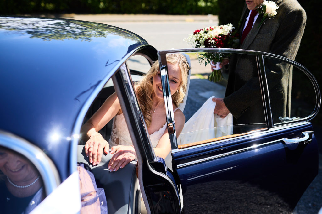 Bride looking out from the back seat of the classic blue Jaguar wedding car