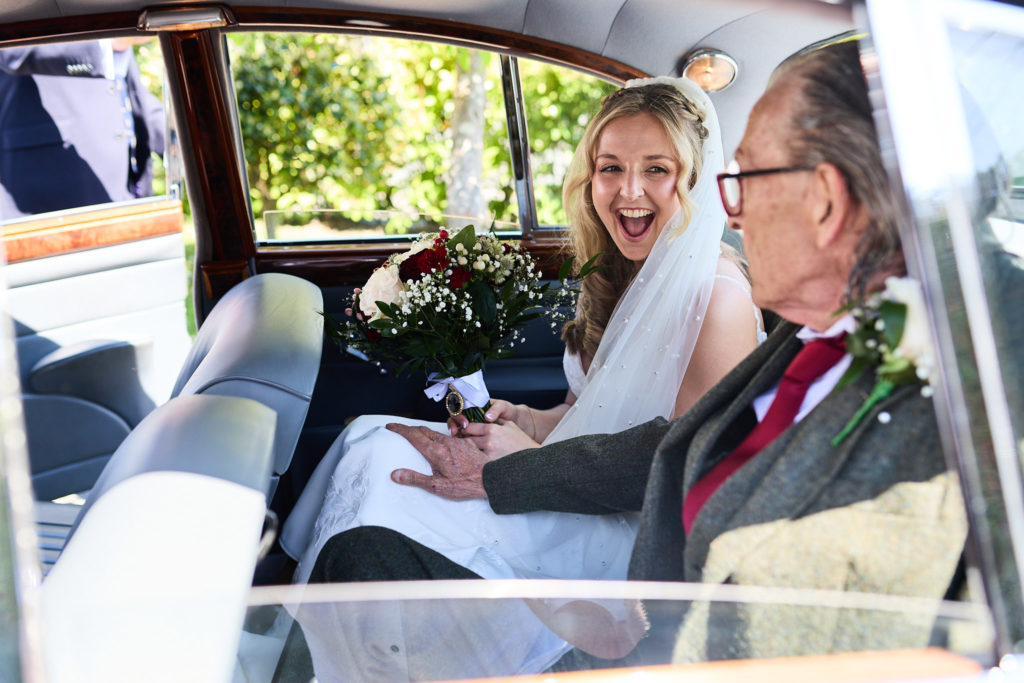 Bride laughing in the back of the wedding car beside an older man in a tweed suit