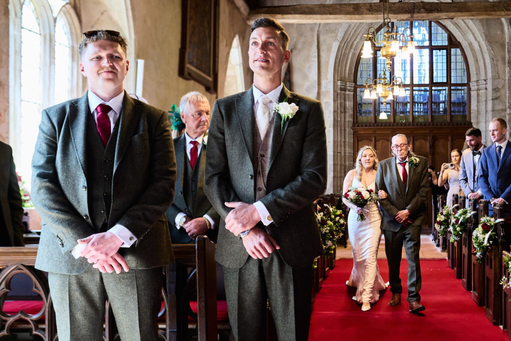 Groom and best man waiting at the front as the bride walks up the church aisle behind them