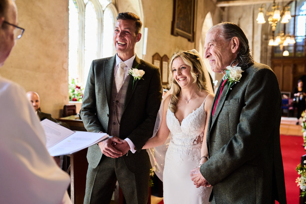 Bride and groom smiling at the vicar during their wedding ceremony at Canewdon church