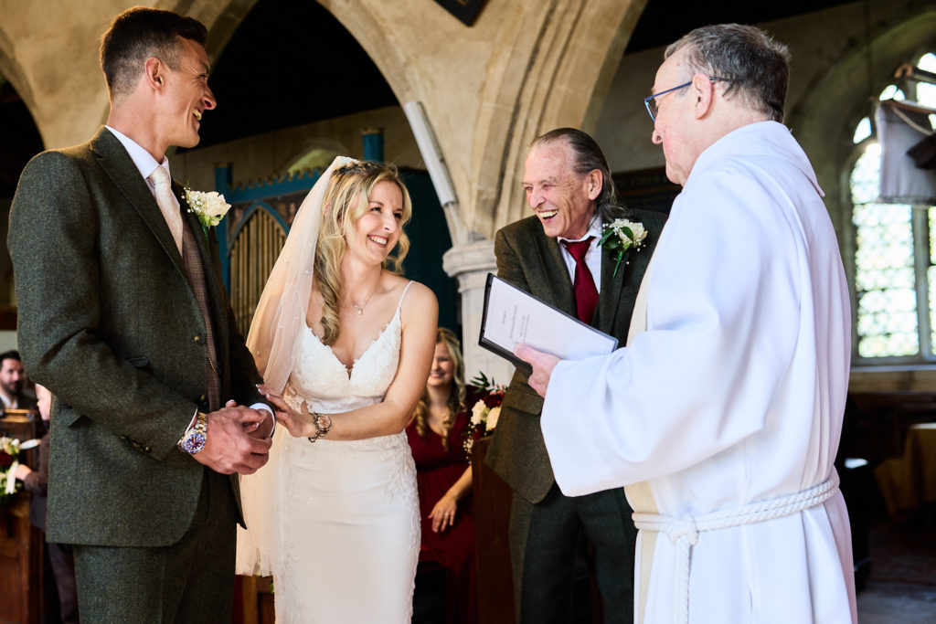 Bride and groom holding hands in front of the vicar as they say their vows