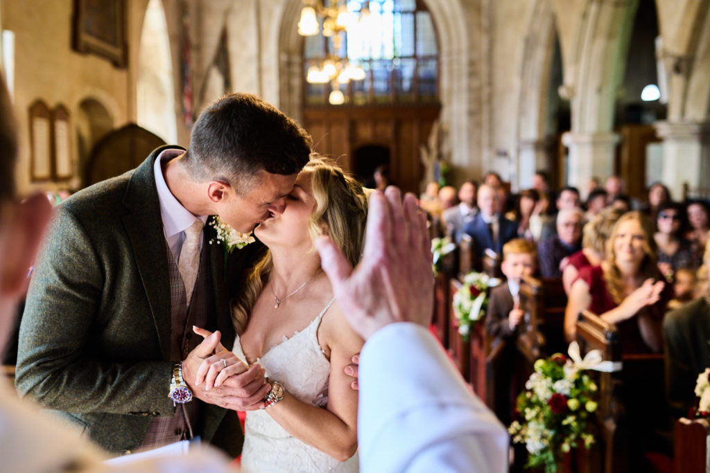Groom kissing the bride with guests watching from the pews