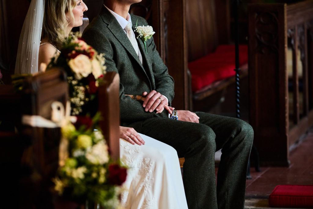 Bride and groom holding hands, seen through the pew-end flowers