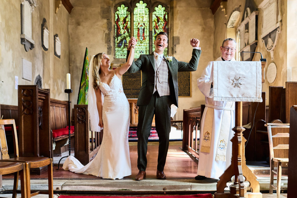 Bride and groom cheering with their arms raised at the altar