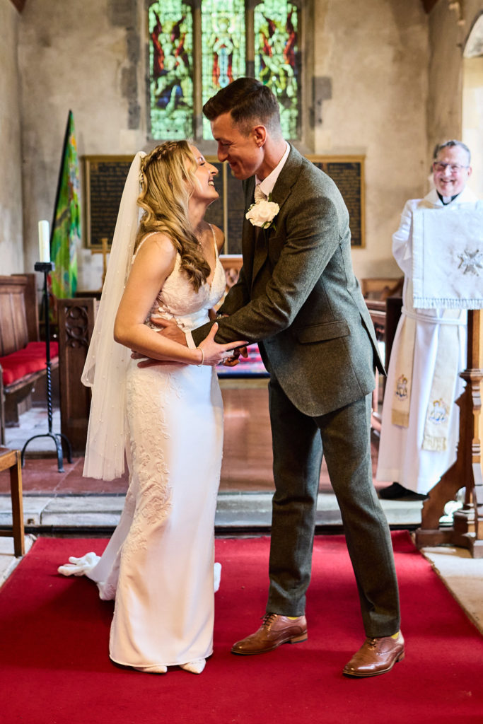 Bride and groom smiling at each other as they hold hands at the altar