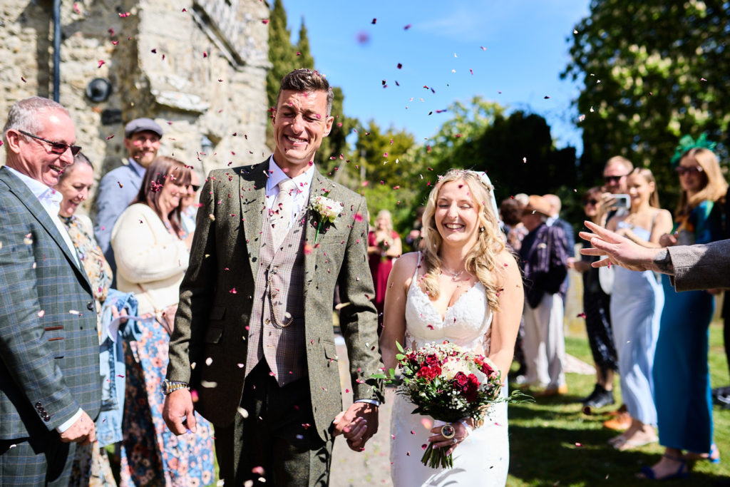 Bride and groom walking through confetti outside St Nicholas Church in Canewdon, near Rochford