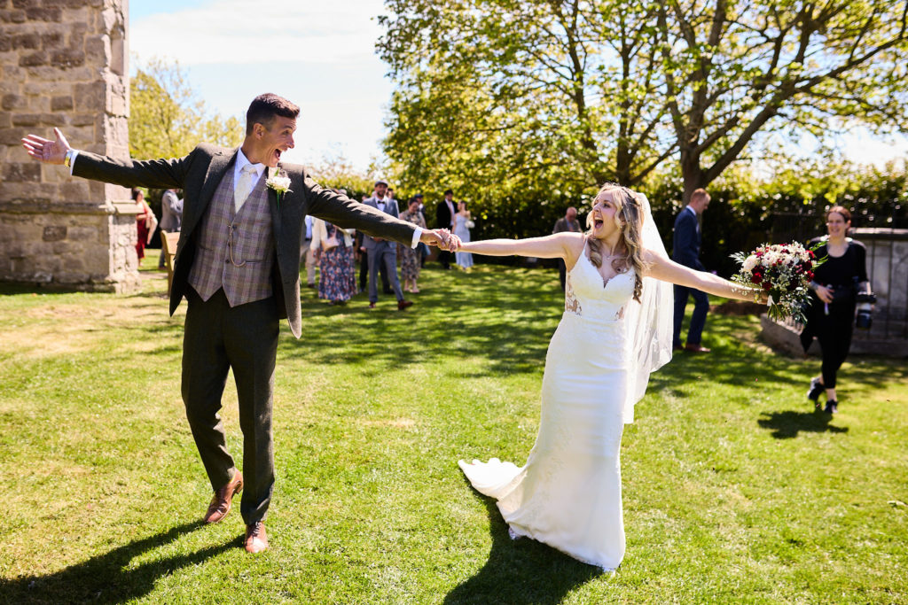 Bride and groom dancing with arms outstretched on the church lawn