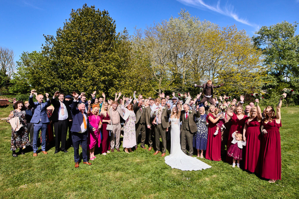 Group photo of all the wedding guests on the church lawn in Canewdon